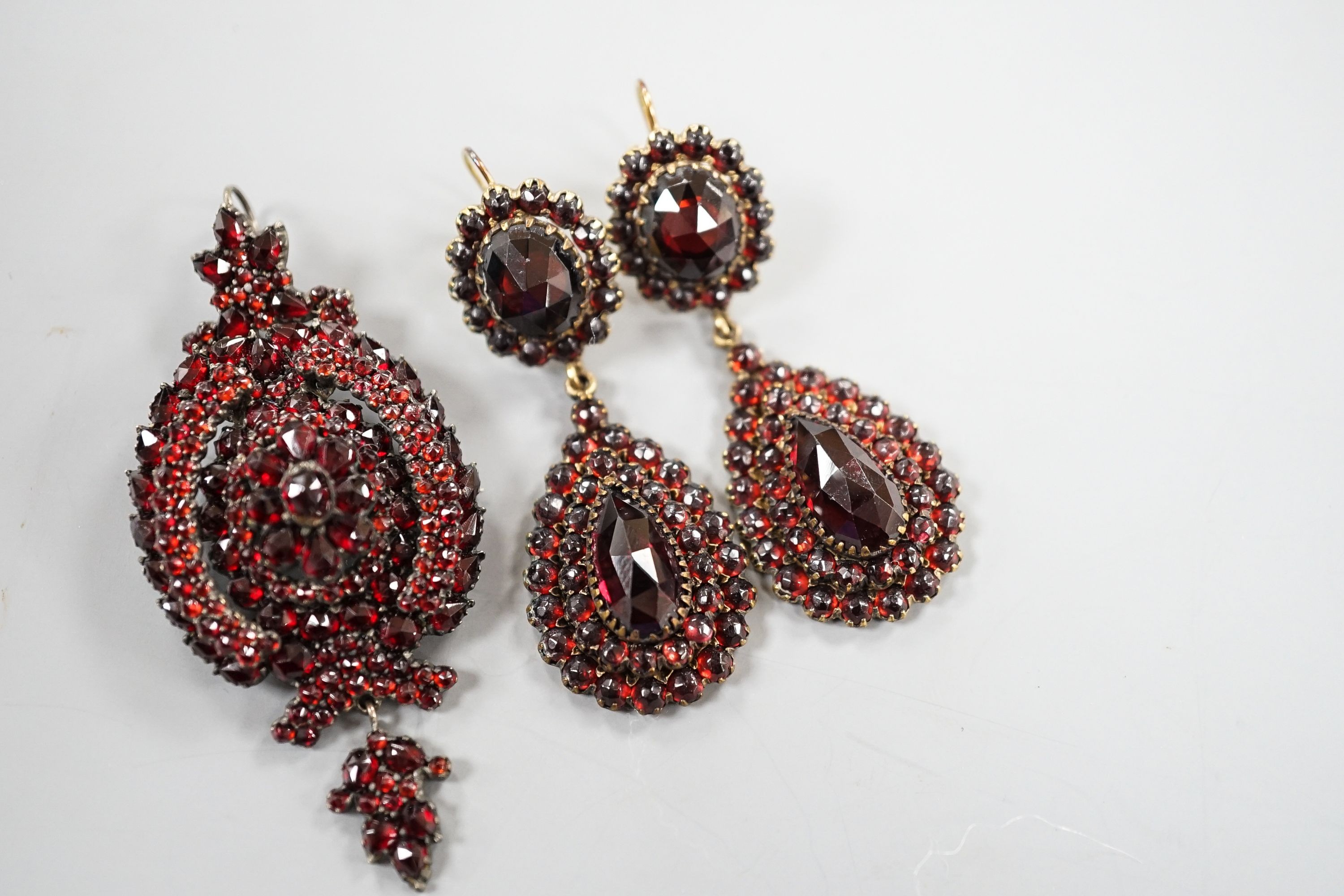 A pair of Victorian gilt metal and facet cut garnet set drop earrings, 51mm and a similar white metal and garnet set pendant brooch.